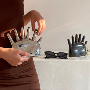 This abstract, one-of-a-kind contemporary jewelry holder by Allthingscurated is designed as an upright-standing palm with 6 fingers for slotting your favorite rings, bracelets or bangles. Made of ceramic and available in silver and black. It measures 19cm or 7.4 inches in width, 16cm or 6.2 inches in height and 14.5cm or 5.7 inches in depth.