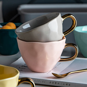 Allthingscurated colorful glazed porcelain cups with gold handle. Designed with a slight all-over concave effect surface that is unique. Available in pink, green, gray, yellow and teal with a capacity of 360ml or 12 ounce.