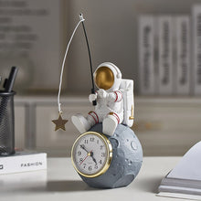 Load image into Gallery viewer, Allthingscurated Desk Clock featuring an astronaut sitting atop a moon rock fishing a star.  Astronaut is dressed in a white space suit with a gold space mask, holding a fishing rod with a dangling gold star. Size of clock measuring height 24cm, width 10cm and length 10cm and weighing 415 gram.
