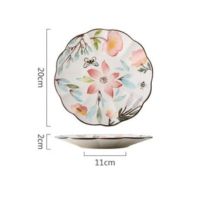 Allthingscurated’s Camille dinnerware features hand-painted florals, fauna and pretty butterflies and a color scheme of pink, yellow, blue,green and brown against a white ceramic background. Every plate is designed with a brown-lined scallop edge. This plate is 8 inches or 20cm.
